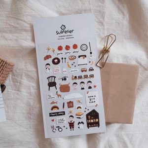 May include: A sheet of stickers with a variety of cute illustrations, including a train, a house, a chair, a camera, a deer, a polar bear, a clock, a cup of coffee, a banana, a pumpkin, a book, a bicycle, and more. The stickers are on a white background and have a brown and orange color scheme. The text on the stickers includes "smile", "sorry", "okay", "have a good time", "that's okay", and "I can do it".