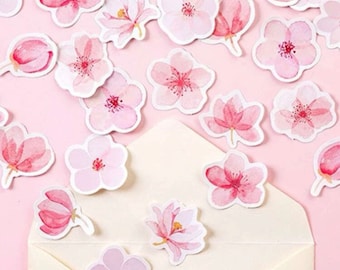 May include: A collection of pink watercolor flower stickers. The stickers are arranged in a random pattern on a light pink background. Some of the stickers are inside a white envelope.
