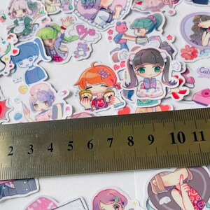 May include: A sheet of colourful stickers featuring cartoon characters with different expressions and poses. The stickers are arranged on a white surface with a ruler measuring 13 centimetres.
