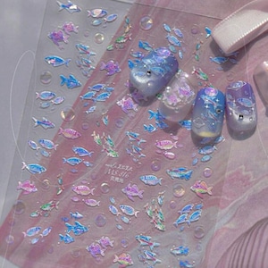 Könnte beinhalten: Transparente Nagelkunst-Aufkleber mit schillernden Fischen und Blasen. Die Aufkleber haben einen holografischen Effekt, wobei sich die Farben von Blau über Lila bis Rosa verändern. Das Bild zeigt auch mehrere dekorierte Nägel mit ähnlichen Wasserdesigns. Der Text "MS 816" ist sichtbar.