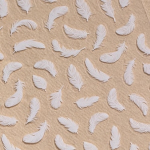 Pode incluir: Enfeites brancos em forma de pena espalhados sobre uma superfície bege. As penas têm um design texturizado e em relevo, criando um efeito 3D. Ideal para projetos de artesanato, o design tem um aspeto delicado e arejado. Para decoração.