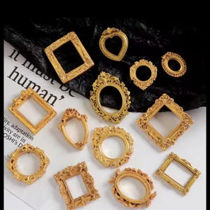 Pode incluir: Uma coleção de doze pequenas molduras douradas ornamentadas em várias formas, incluindo designs retangulares, ovais e em forma de coração. Cada moldura apresenta detalhes em relevo intrincados nas bordas e um centro oco.
