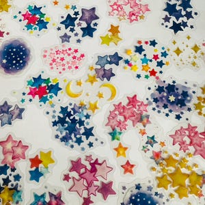 May include: A sheet of colorful star stickers with watercolor accents. The stickers feature various shades of blue, pink, yellow, and purple. Some stickers have a crescent moon shape.