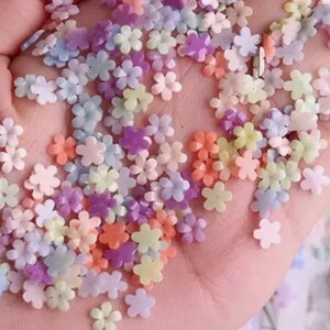 K&ouml;nnte beinhalten: Eine Sammlung von pastellfarbenen, blumenf&ouml;rmigen Streuseln. Die Streusel sind in verschiedenen Farben, darunter rosa, lila, blau und gelb.