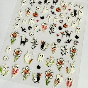 May include: A clear sheet of adhesive stickers featuring various Halloween-themed illustrations including white ghosts, black cats, orange pumpkins, skulls, flowers, bats, and candles. The designs are arranged in a grid pattern on a transparent backing.