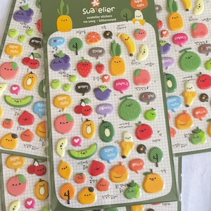 May include: A set of four sheets of colorful fruit-themed stickers. Each sheet features a grid of stickers with different fruits, including apples, bananas, cherries, pineapples, and melons. The stickers have a 3D puffy texture and feature cute cartoon faces.
