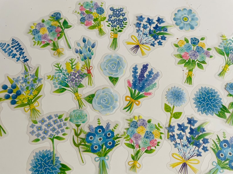 May include: A sheet of colorful floral stickers with blue, white, and green flowers. The stickers are arranged in a variety of bouquets and individual flowers.