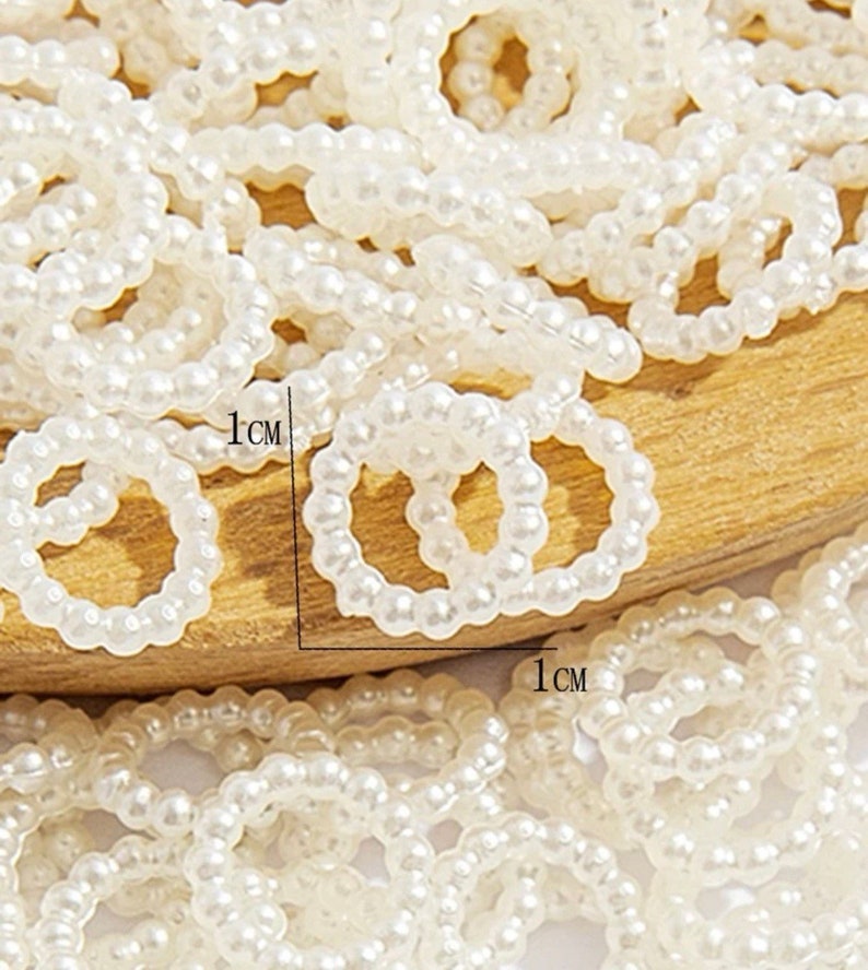 K&ouml;nnte beinhalten: Nahaufnahme einer gro&szlig;en Menge wei&szlig;er Perlenringe. Die Ringe haben einen Durchmesser von etwa 1 cm.