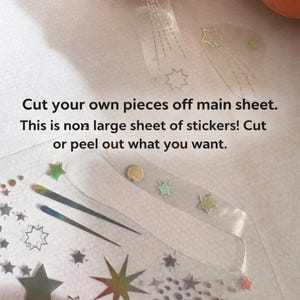 May include: Clear sticker sheet with various star and comet designs in iridescent colors. The text reads: "Cut your own pieces off main sheet. This is non large sheet of stickers! Cut or peel out what you want."