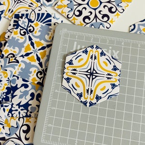 May include: A hexagonal tile with a blue, white, and yellow geometric pattern. The tile is on a gray cutting mat with a grid pattern.