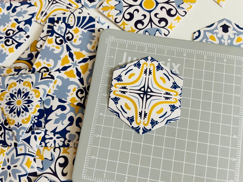 May include: A hexagonal tile with a blue, white, and yellow geometric pattern. The tile is on a gray cutting mat with a grid pattern.
