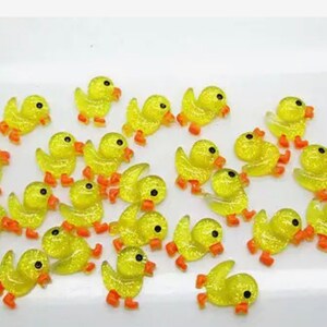 K&ouml;nnte beinhalten: Eine Sammlung von gelben Glitzer-Enten-Anh&auml;ngern mit orangefarbenen Schn&auml;beln und F&uuml;&szlig;en. Die Anh&auml;nger sind perfekt, um Kunsthandwerk, Schmuck und anderen Projekten einen Hauch von Verspieltheit zu verleihen.