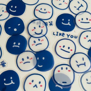May include: A collection of blue and white stickers with various smiley faces and text. The stickers feature different expressions, including happy, sad, and surprised. The text on the stickers includes "Like You" and "白事 可爱".