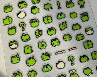 May include: A clear sticker sheet featuring numerous small, individual green frog illustrations in various poses and expressions, including some with exclamation points, question marks, and pink tongues, all outlined in black.