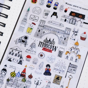 K&ouml;nnte beinhalten: Eine Blatt mit Aufklebern mit Schwarzwei&szlig;-Illustrationen von Moskauer Sehensw&uuml;rdigkeiten, darunter der Kreml, die Basilius-Kathedrale und der Rote Platz. Die Aufkleber zeigen auch traditionelle russische Matrjoschka-Puppen, ein Reh, einen Cupcake und ein Schild mit der Aufschrift "Moskau".