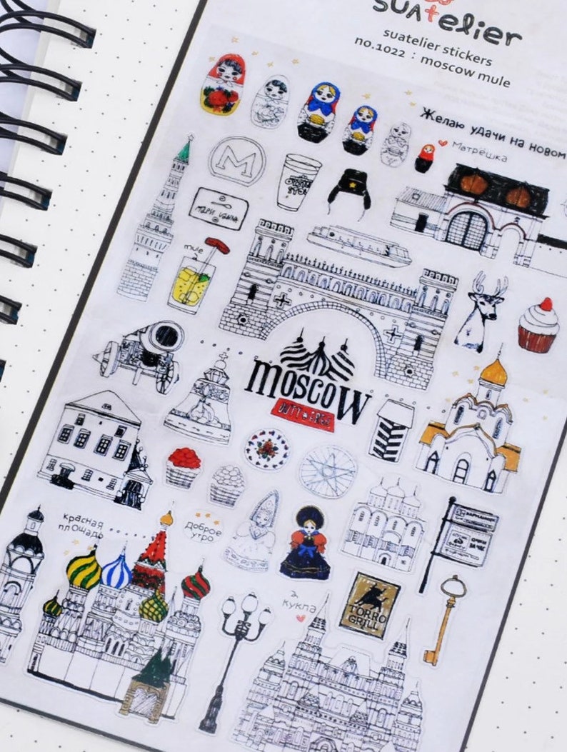 K&ouml;nnte beinhalten: Eine Blatt mit Aufklebern mit Schwarzwei&szlig;-Illustrationen von Moskauer Sehensw&uuml;rdigkeiten, darunter der Kreml, die Basilius-Kathedrale und der Rote Platz. Die Aufkleber zeigen auch traditionelle russische Matrjoschka-Puppen, ein Reh, einen Cupcake und ein Schild mit der Aufschrift "Moskau".