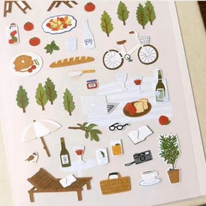 May include: A sheet of colorful stickers featuring various picnic and outdoor themed illustrations. The stickers include a bicycle, trees, a baguette, a picnic basket, a glass of wine, a camera, a lounge chair, and more.