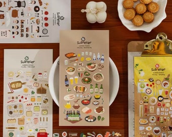 May include: Three sheets of stickers featuring illustrations of food and drinks. The stickers are on a brown background with white text that reads "Suatelier" and "Suatelier stickers" along with the name of the sticker set. The stickers are arranged on a wooden table with a white plate of biscuits and a clipboard with a yellow sheet of paper with more stickers.