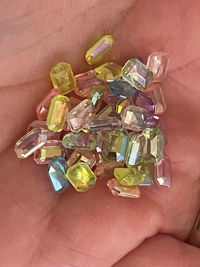 K&ouml;nnte beinhalten: Sortiment aus irisierenden, facettierten, rechteckigen Glasperlen in verschiedenen Gr&uuml;nt&ouml;nen, Gelb, Rosa und Lila.