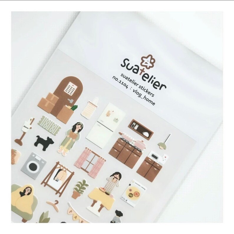 K&ouml;nnte beinhalten: Eine Bogen mit Aufklebern, die Illustrationen eines Hausinneren zeigen, darunter M&ouml;bel, Ger&auml;te und Personen. Die Aufkleber sind in einem hellbraunen, rosa und wei&szlig;en Farbschema gehalten. Der Bogen ist mit "Suatelier stickers no.1104 : vlog_home" beschriftet.