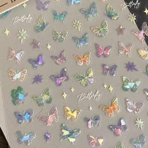 May include: Sheet of iridescent butterfly stickers in various colors, including pink, blue, green, and yellow. The stickers have a holographic effect and are arranged with star-shaped and diamond-shaped accents. The word "Butterfly" is written in cursive.