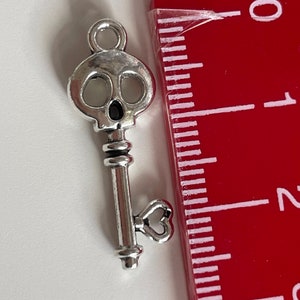 Op de afbeelding: Zilveren schedel sleutelbedel met een hartvormige lus aan de onderkant. De sleutel is ongeveer 2,5 cm lang.