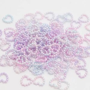 K&ouml;nnte beinhalten: Ein gro&szlig;er Haufen aus schimmernden, pastellfarbenen, rosa, lila und blauen Perlen in Herzform.