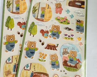 May include: A sheet of stickers featuring illustrations of bears in various activities, including sleeping, playing, and exploring the outdoors. The stickers are in a cartoon style with a whimsical and colorful design. The text on the sheet reads "くまのB曜日".