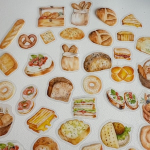 Puede incluir: Una colección de ilustraciones de acuarela de varios panes, pasteles y sándwiches. Las ilustraciones están sobre un fondo blanco e incluyen una variedad de formas y tamaños, como baguettes, bollos, croissants y sándwiches.