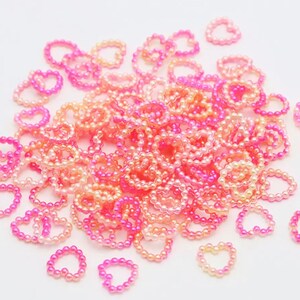 K&ouml;nnte beinhalten: Ein gro&szlig;er Haufen rosa und pfirsichfarbener herzf&ouml;rmiger Perlen. Die Perlen sind in einem Farbverlauf von rosa zu pfirsich angeordnet.