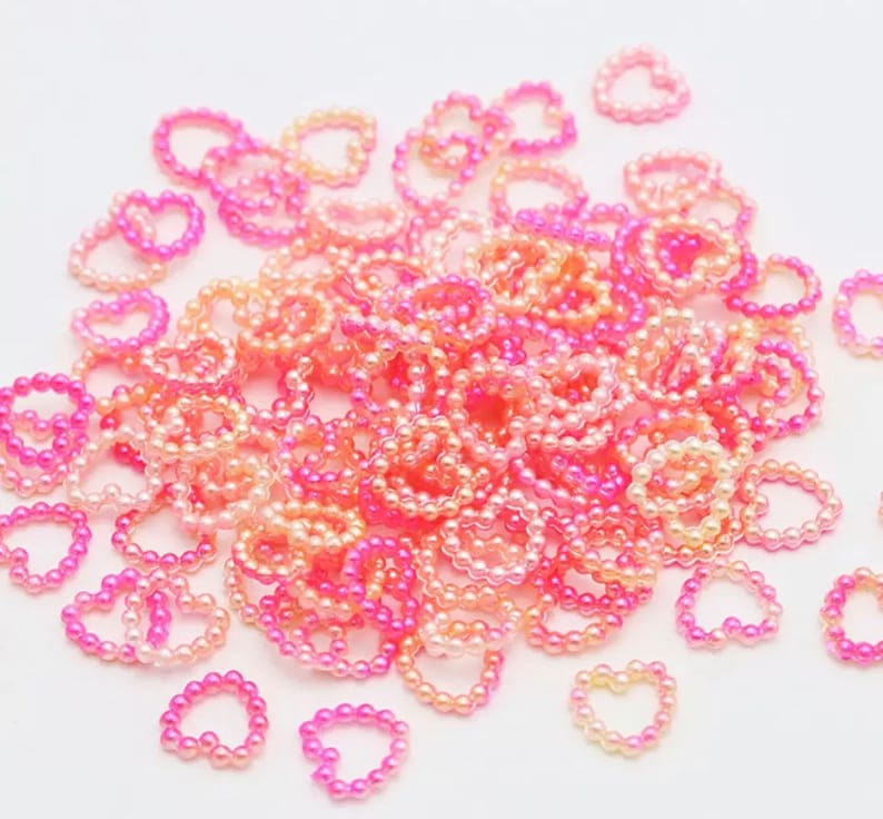 K&ouml;nnte beinhalten: Ein gro&szlig;er Haufen rosa und pfirsichfarbener herzf&ouml;rmiger Perlen. Die Perlen sind in einem Farbverlauf von rosa zu pfirsich angeordnet.