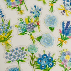 May include: A sheet of blue and green floral stickers. The stickers feature various bouquets of flowers, including roses, hydrangeas, and forget-me-nots. The stickers are perfect for adding a touch of whimsy to journals, planners, and other craft projects.
