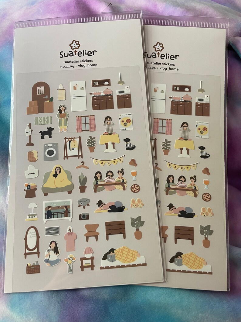 K&ouml;nnte beinhalten: Zwei Bl&auml;tter mit Aufklebern, die Illustrationen eines Hauses, von M&ouml;beln und Menschen zeigen. Die Aufkleber befinden sich auf einem hellgrauen Hintergrund und tragen den Text "Suatelier" und "no.1304 : vlog_home".