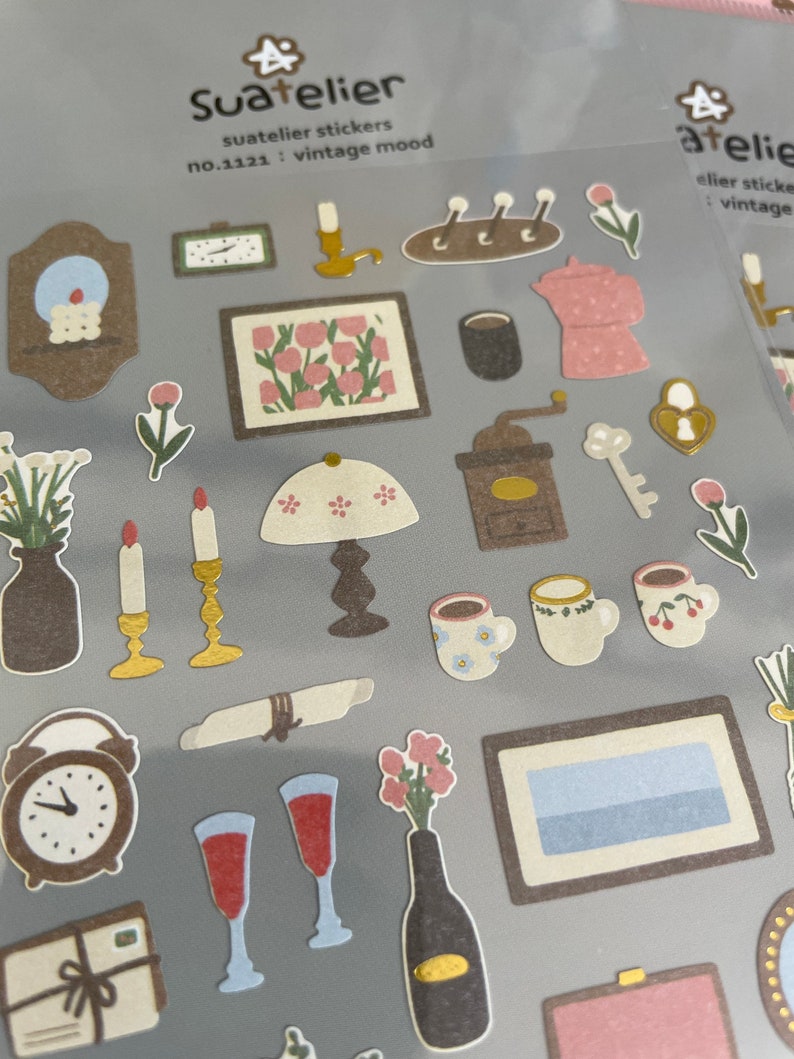 May include: A sheet of vintage-themed stickers featuring illustrations of a coffee grinder, candles, a lamp, a clock, a bottle of wine, a picture frame, a teapot, and other items. The stickers are labelled "Suatelier stickers no.1121: vintage mood".
