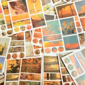 May include: A selection of aesthetic paper stickers with landscape and nature-themed designs. The stickers display images of sunsets, flowers, and scenic views in warm, earthy tones. Some stickers have circular designs.