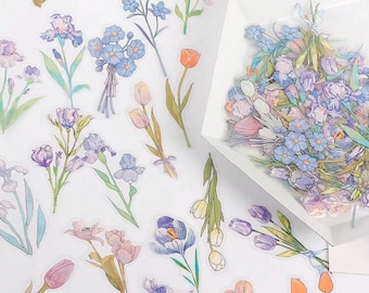 May include: A sheet of clear stickers featuring various floral designs. The stickers include blue forget-me-nots, pink tulips, purple irises, and orange tulips.