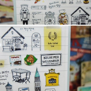 K&ouml;nnte beinhalten: Eine Bogen mit Aufklebern, die Illustrationen von deutschem Essen, Getr&auml;nken und Sehensw&uuml;rdigkeiten zeigen. Die Aufkleber sind auf durchsichtigem, transparentem Papier gedruckt und haben einen wei&szlig;en Hintergrund. Die Aufkleber enthalten Bilder von Brezeln, Bierkr&uuml;gen, einem Lebkuchenhaus, einem Schloss und einem Schild mit der Aufschrift "Ich liebe Sie" (Ich liebe dich).