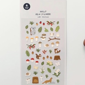 Puede incluir: Una hoja de pegatinas con una variedad de criaturas y plantas del bosque, incluyendo un koala, una ardilla, setas, caracoles, bayas, hojas y flores. Las pegatinas están sobre un fondo blanco y tienen un borde azul claro. El texto "DAILY DECO STICKERS" y "1188: Little Forest" está impreso en la hoja.