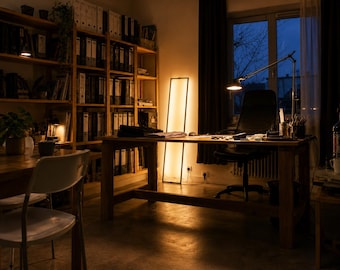 May include: A home office with a wooden desk, chair, and bookshelves. A tall, rectangular lamp and a desk lamp provide warm lighting. The room has a window with a view of a dark, tree-lined sky.