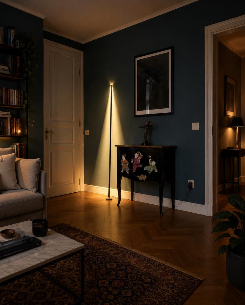 Puede incluir: Una l&aacute;mpara de pie negra moderna con un dise&ntilde;o vertical, que emite una luz c&aacute;lida y enfocada. La l&aacute;mpara se encuentra en una habitaci&oacute;n con paredes de color verde azulado oscuro, una alfombra estampada y un mueble decorativo. El ambiente es acogedor.