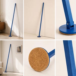 Puede incluir: L&aacute;mpara de pie moderna y minimalista en un vibrante color azul. La l&aacute;mpara presenta un poste delgado y rectangular que se extiende hacia arriba desde una base circular. La base tiene una parte inferior de corcho. La l&aacute;mpara est&aacute; dise&ntilde;ada para apoyarse contra una pared.