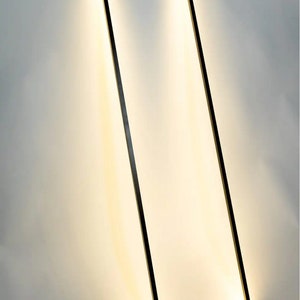 Side view of leaning floor lamp with warm ambient light in cozy modern corner. Geometric frame adds a sculptural element to any interior