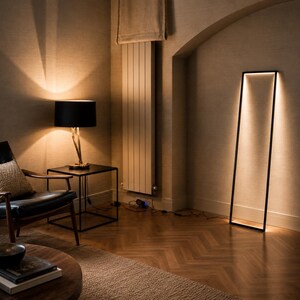 Pode incluir: Uma sala de estar moderna com um candeeiro de p&eacute; preto e um candeeiro de mesa. O candeeiro de p&eacute; tem uma estrutura retangular com luz brilhante. O candeeiro de mesa tem uma sombra preta e uma base dourada. Uma cadeira preta e uma mesa de madeira tamb&eacute;m est&atilde;o presentes.