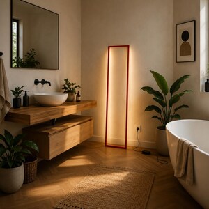 Pode incluir: Uma casa de banho moderna com uma lumin&aacute;ria de ch&atilde;o retangular com moldura vermelha que emite luz quente. O quarto apresenta uma vaidade de madeira com uma pia branca, uma banheira e plantas em vasos. O ch&atilde;o &eacute; de madeira.