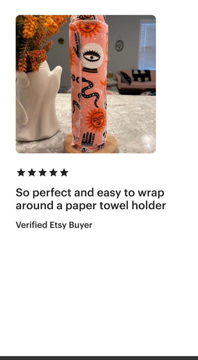 May include: A cylindrical fabric roll featuring a repeating pattern of black and orange celestial motifs, including suns, moons, crystal balls, and hands on a light pink background, secured with visible stitching along the vertical edge.