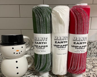 May include: Three rolls of unpaper towels, each with a different color: green, white, and red. The labels on the rolls read "Manic Earth Unpaper Towels 12 Pack Hand Made".