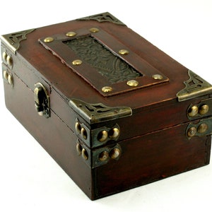 May include: A dark brown wooden box with ornate brass accents and a hinged lid. The box has a decorative metal inlay on the top and is secured with a brass latch.