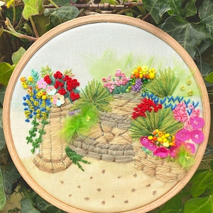Puede incluir: Arte de bordado en aro que representa una escena de jardín con un muro de piedra, plantas verdes y flores de colores. Las flores están hechas con hilo de bordar de colores y cuentas.
