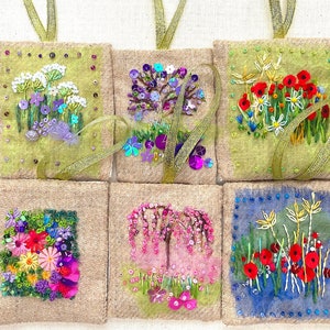 May include: Six small burlap pouches with embroidered floral designs. Each pouch features a different floral motif, including a purple flower, a pink flower, a red flower, and a yellow flower. The pouches are all tied with gold ribbon.