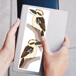 Könnte beinhalten: Ein Aufkleber mit zwei Kookaburras im Cartoon-Stil, die auf einem Ast sitzen. Die Kookaburras sind braun, weiß und blau mit schwarzen Augen. Der Hintergrund ist weiß.